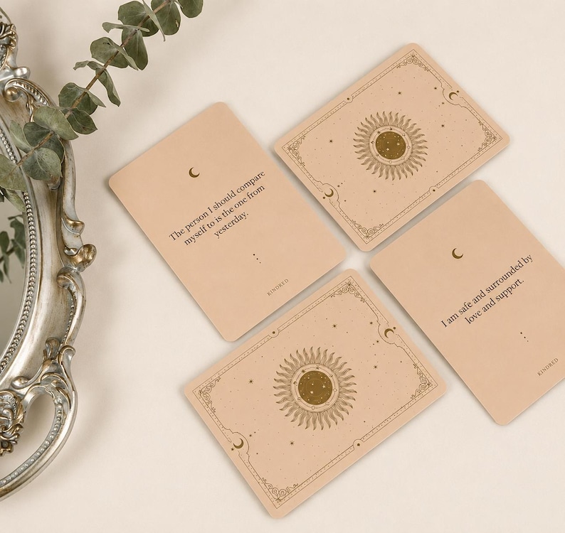 May include: Four beige oracle cards with celestial designs and text. Each card features a sunburst design, crescent moons, and decorative borders. The cards have phrases like "The person I should compare myself to is the one from yesterday."
