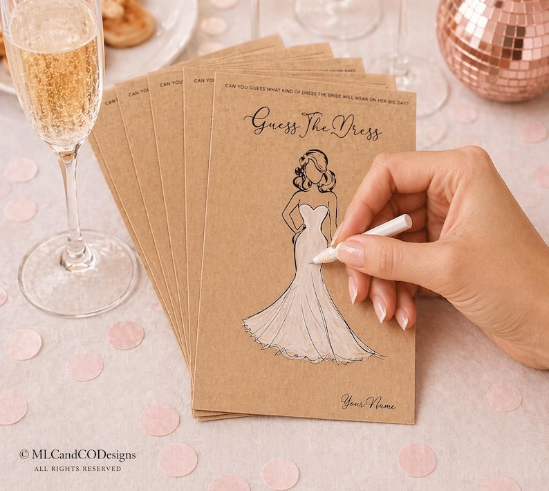 May include: A pile of kraft paper bridal shower game cards with the text "Guess The Dress" and a drawing of a wedding dress. A hand is holding a white pen, ready to write. A glass of champagne is in the foreground.