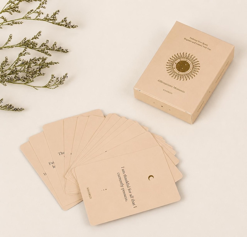 May include: A beige affirmation card deck with a matching box. The box features a sunburst design and the words "Affirmations Moments" and "Embrace Your Spirit, Brighten and Follow Your Star." Several cards are fanned out, with text including "I am thankful for all that I currently possess."