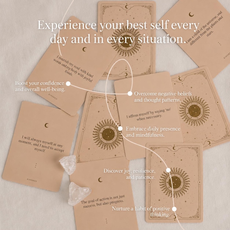 May include: A collection of beige affirmation cards with celestial designs and text. The cards feature sun and moon illustrations, with phrases like "Experience your best self" and "Boost your confidence". Clear quartz crystals are also present.