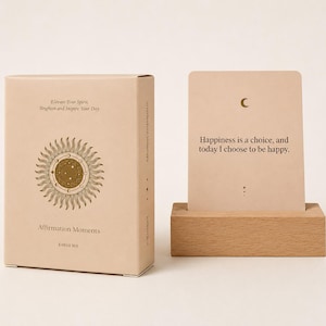 May include: A beige box and card set with the text "Elevate Your Spirit, Brighten and Inspire Your Day" and "Affirmation Moments." The card reads "Happiness is a choice, and today I choose to be happy." A wooden card holder is in the image.