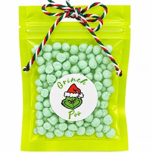 May include: A lime green resealable plastic pouch filled with small, light green candy pieces. A round white sticker on the front features a green character wearing a red Santa hat with the text Grinch Poo. The bag is tied with red, white, and green twine.