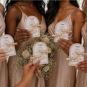 May include: Five sets of two hair clips with gold-toned metal alligator clasps and white resin pieces containing gold flakes. Each set is attached to an arched white card featuring the text To Have and To Hold your hair back.