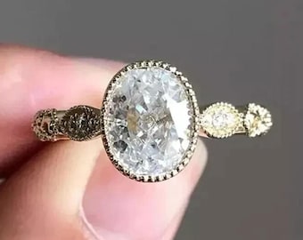 May include: A gold ring featuring a large, oval-cut, clear faceted center stone surrounded by a beaded metal border. The band is crafted with intricate, textured, marquise-shaped metal segments that extend along the sides of the ring.