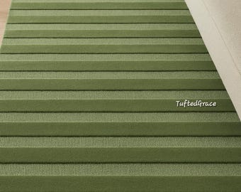 May include: A green rectangular rug with a striped design. The rug features alternating bands of textured and patterned sections. The rug is placed on a wooden floor. The text "TuftedGrace" is visible on the rug. The rug's dimensions are in centimetres.