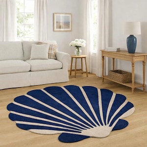 Könnte beinhalten: Ein muschelförmiger Teppich in Marineblau und Creme in einem Wohnzimmer. Das Design des Teppichs ahmt eine Muschel nach, wobei Marineblau die äußere Form bildet und cremefarbene Linien von der Basis ausstrahlen. Der Teppich liegt auf einem Holzboden.