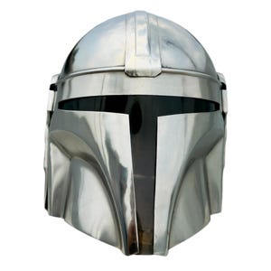 May include: A polished silver-colored metal helmet featuring a smooth, rounded dome and a T-shaped black visor. The helmet has a reflective surface with contoured cheek plates and a central ridge running vertically along the top of the headpiece.