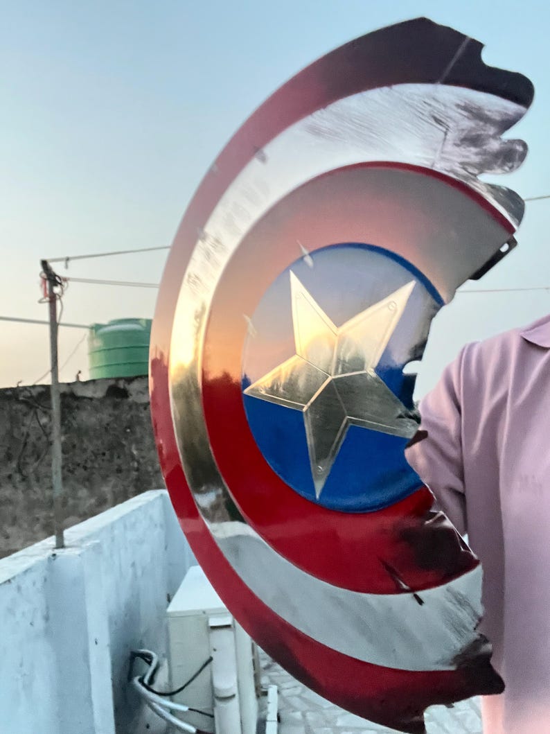 Peut inclure: Un bouclier Captain America avec une finition m&eacute;tallique. Le bouclier pr&eacute;sente un cercle bleu avec une &eacute;toile dor&eacute;e au centre, entour&eacute; de rayures rouges et blanches. Le bouclier a une apparence us&eacute;e et ab&icirc;m&eacute;e.