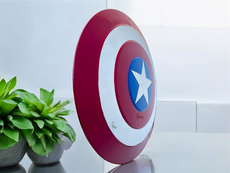May include: A red, white, and blue shield with a star emblem. The shield is round with a red outer ring, a white inner ring, and a blue center with a white star. The shield is a prop.