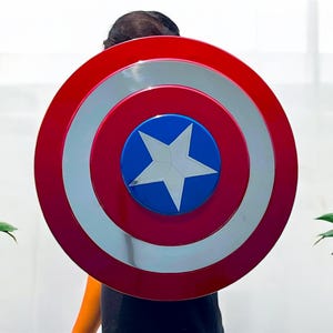 May include: A red, white, and blue shield with a star in the center. The shield has a circular design with concentric rings of red, silver, and red. The center is blue with a white star.