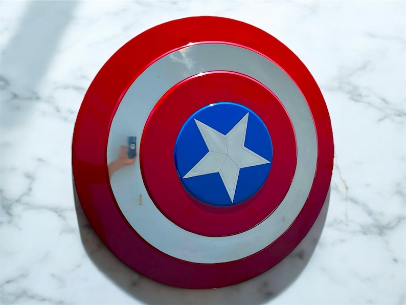 May include: A red, white, and blue shield with a star in the center. The shield has a circular design with concentric rings of red, white, and red. The center is blue with a white star.