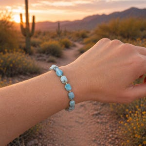 May include: A beaded bracelet featuring smooth, tumbled light blue stones with white marbling, interspersed with small, round, metallic gold-toned spacer beads. The stones are irregular in shape and arranged in a single strand on an elastic cord.