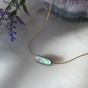 May include: A delicate gold-toned chain necklace featuring a single, rectangular abalone shell pendant. The pendant displays an iridescent surface with swirling hues of blue, green, and gold, suspended on a thin, polished metallic link chain.