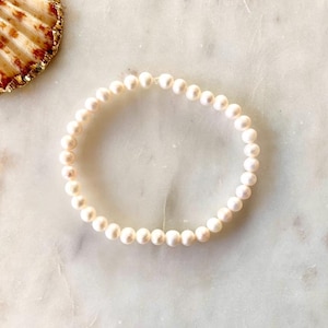 May include: A circular bracelet composed of small, uniform, off-white spherical pearls strung together. The pearls have a smooth, lustrous finish and are arranged in a continuous loop, creating a simple and classic piece of jewelry.