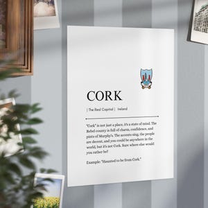 May include: A white poster featuring the word "CORK" in black, with "The Real Capital | Ireland" beneath. An emblem is above the text. The poster includes a quote about Cork and the phrase "Haunted to be from Cork."