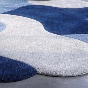 May include: A modern area rug with a flowing, organic design. The rug features a pattern of swirling shapes in shades of blue and white, creating a soft, textured surface. The rug's design adds a contemporary touch to any room.