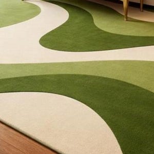 May include: A rectangular area rug with a flowing, abstract design. The rug features a cream-colored background with wavy patterns in shades of green. The rug is placed on a wooden floor.