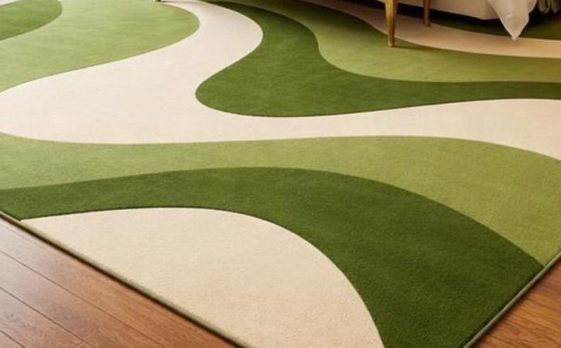 May include: A rectangular area rug with a flowing, abstract design. The rug features a cream-colored background with wavy patterns in shades of green. The rug is placed on a wooden floor.