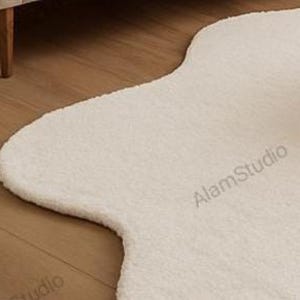 Cream irregular shape rug with a soft, cloud-like form in a minimalist living room. Hand-tufted wool adds cozy texture. Neutral tones, wood furniture, and modern decor create a warm, Japandi-inspired aesthetic.