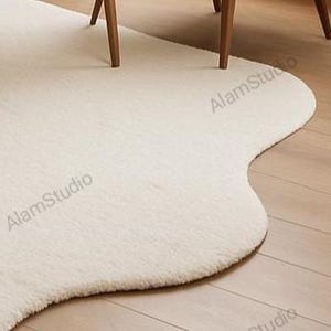 Cream irregular shape rug with a soft, cloud-like form in a minimalist living room. Hand-tufted wool adds cozy texture. Neutral tones, wood furniture, and modern decor create a warm, Japandi-inspired aesthetic.