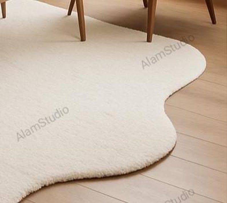 Cream irregular shape rug with a soft, cloud-like form in a minimalist living room. Hand-tufted wool adds cozy texture. Neutral tones, wood furniture, and modern decor create a warm, Japandi-inspired aesthetic.
