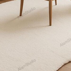 Cream irregular shape rug with a soft, cloud-like form in a minimalist living room. Hand-tufted wool adds cozy texture. Neutral tones, wood furniture, and modern decor create a warm, Japandi-inspired aesthetic.