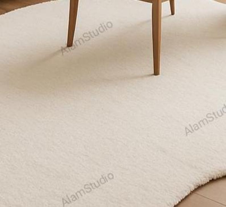 Cream irregular shape rug with a soft, cloud-like form in a minimalist living room. Hand-tufted wool adds cozy texture. Neutral tones, wood furniture, and modern decor create a warm, Japandi-inspired aesthetic.