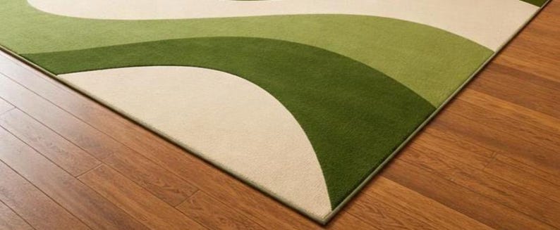 May include: A green, cream, and light green area rug with a wave design. The rug is placed on a hardwood floor. The rug's design features curved lines and a soft texture, adding a decorative element to the room.