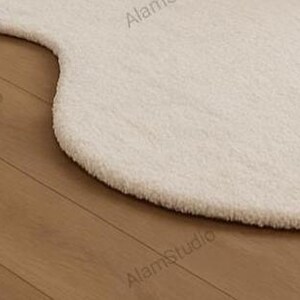 Cream irregular shape rug with a soft, cloud-like form in a minimalist living room. Hand-tufted wool adds cozy texture. Neutral tones, wood furniture, and modern decor create a warm, Japandi-inspired aesthetic.