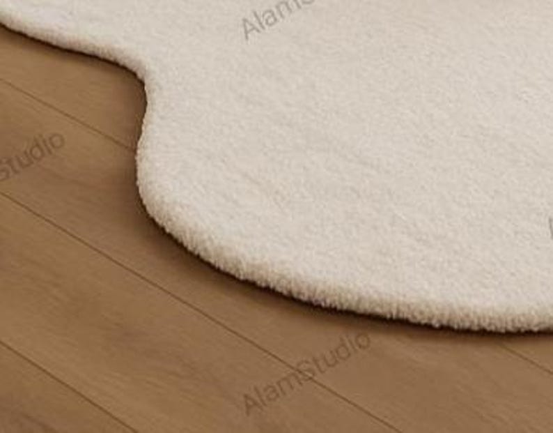 Cream irregular shape rug with a soft, cloud-like form in a minimalist living room. Hand-tufted wool adds cozy texture. Neutral tones, wood furniture, and modern decor create a warm, Japandi-inspired aesthetic.