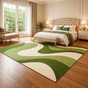 May include: A bedroom with a large green, white, and light green patterned rug. The rug is in front of a bed with a beige headboard and a green bedspread. A beige bench sits at the foot of the bed. The room has hardwood floors and a large window.