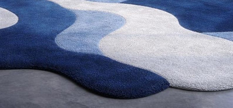 May include: A close-up of a blue and white area rug with a wavy design. The rug features shades of dark blue, light blue, and white, creating a textured, flowing pattern. The rug is made of a soft, plush material.