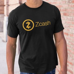 May include: Black t-shirt with the Zcash logo in gold. The logo shows a stylized "Z" within a gold circle, and the word "Zcash" is printed in gold to the right. The shirt is made of a soft material.