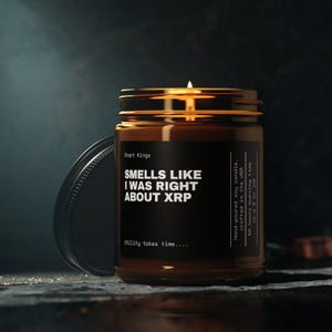 May include: A lit soy candle in a glass jar with a gold lid. The black label reads "SMELLS LIKE I WAS RIGHT ABOUT XRP" and "Chart Kings". The candle is hand-poured in the USA and has a 50-hour burn time.