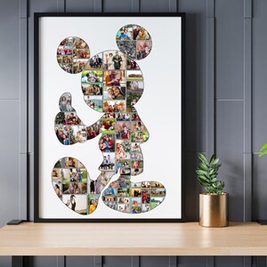 May include: A framed Mickey Mouse silhouette art print filled with numerous small photos. The black frame surrounds the white background, and the artwork is displayed on a wooden shelf. A small potted plant sits nearby.