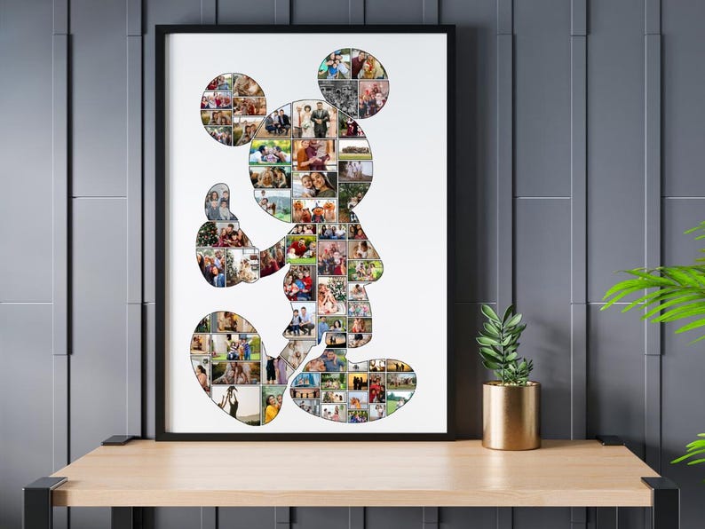 May include: A framed Mickey Mouse silhouette art print filled with numerous small photos. The black frame surrounds the white background, and the artwork is displayed on a wooden shelf. A small potted plant sits nearby.