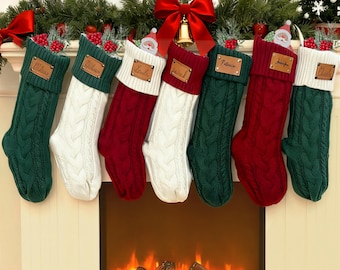 以下が含まれることがあります： 緑、白、赤のケーブルニットのクリスマスストッキング6つ。各ストッキングにはパーソナライズされた革製のタグが付いています。暖炉の上に飾られ、緑と赤いリボンで飾られ、お祝いの雰囲気を醸し出しています。