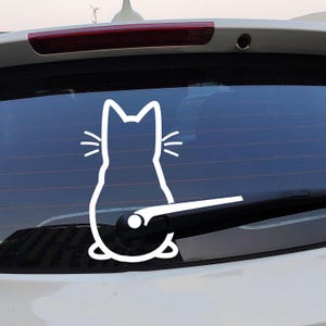 May include: White cat silhouette sticker, viewed from the back, with whiskers. The decal is affixed to a car's rear window, positioned above the wiper blade.