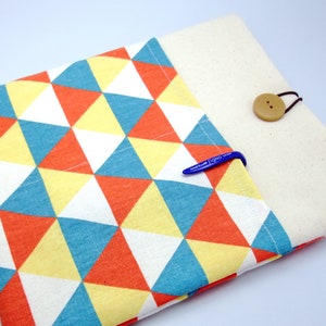 Puede incluir: Una funda para portátil con un patrón geométrico de triángulos naranja, amarillo, azul y blanco. La funda tiene una solapa con cierre de botón y un forro de tela blanco.