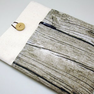 Puede incluir: Una funda para portátil de tela con estampado de madera en marrón y blanco, con una solapa de lona beige y un cierre de botón de madera.
