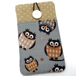 Peut inclure: Une housse de téléphone grise avec un motif de hiboux aux motifs argyle marron et beige. La partie supérieure est beige à pois blancs et une fermeture à bouton blanc. Un cordon élastique noir maintient le bouton.