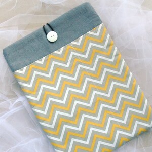 Puede incluir: Una funda para portátil con estampado de chevron gris y amarillo, con una solapa gris y un cierre de botón blanco.