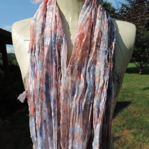 May include: A long, thin scarf made of soft, sheer fabric. The scarf is a mix of pink, blue, and white colors with a subtle, speckled pattern.