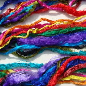 May include: A vibrant display of colorful silk threads in shades of blue, red, purple, green, orange, and yellow. The threads are arranged in a layered, textured pattern, creating a visually rich and dynamic composition. Ideal for craft projects.