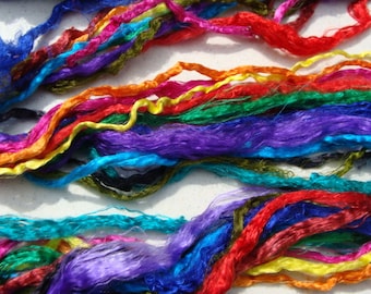 May include: A vibrant display of colorful silk threads in shades of blue, red, purple, green, orange, and yellow. The threads are arranged in a layered, textured pattern, creating a visually rich and dynamic composition. Ideal for craft projects.