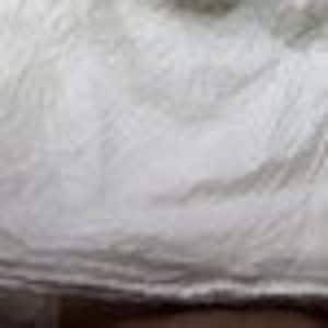 May include: A white fabric material with a visible, crinkled, and textured surface. The material features numerous small, irregular folds and creases throughout, creating a layered and uneven appearance across the entire visible area of the textile.