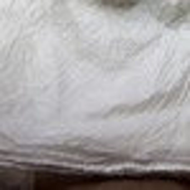 May include: A white fabric material with a visible, crinkled, and textured surface. The material features numerous small, irregular folds and creases throughout, creating a layered and uneven appearance across the entire visible area of the textile.