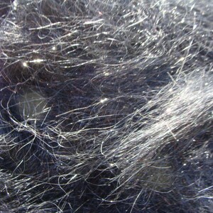 Puede incluir: Primer plano de una tela azul oscuro con una textura brillante e iridiscente. La tela est&aacute; hecha de hilos finos y delgados que crean una apariencia difusa, casi peluda.