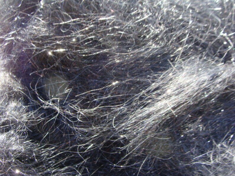 Puede incluir: Primer plano de una tela azul oscuro con una textura brillante e iridiscente. La tela est&aacute; hecha de hilos finos y delgados que crean una apariencia difusa, casi peluda.