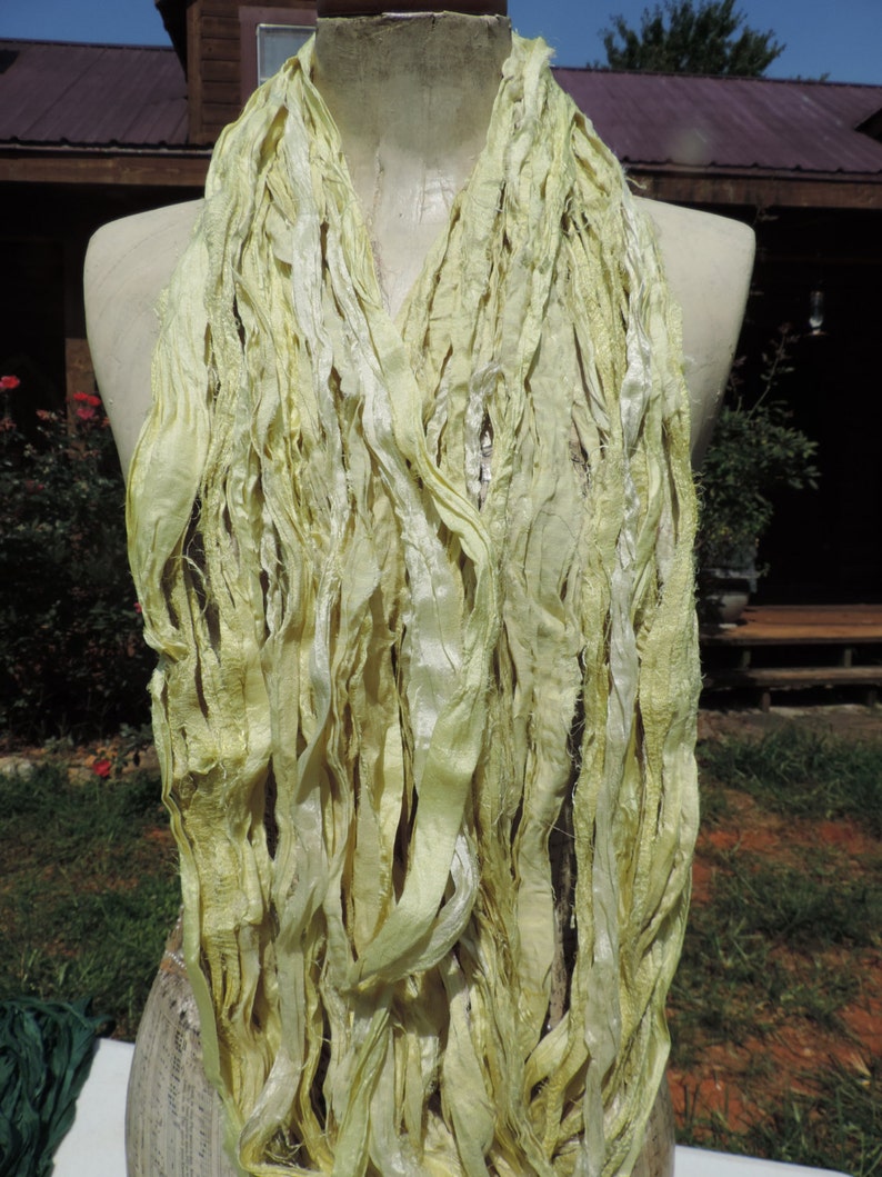 May include: A pale yellow silk scarf made of thin strips of fabric. The scarf is draped around a mannequin's neck.